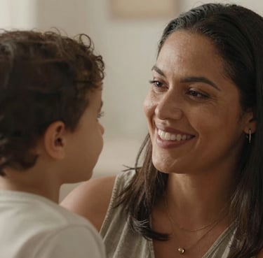 Portrait of a smiling Brazilian mother looking proudly at her child (out of frame), warm and soft lighting, emotional photography style.