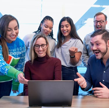 Diverse business team celebrating success while looking at a laptop in a modern office.
