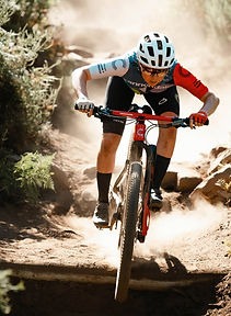 Professional mountain biker racing down a dusty dirt trail on a high-performance cross-country bike.