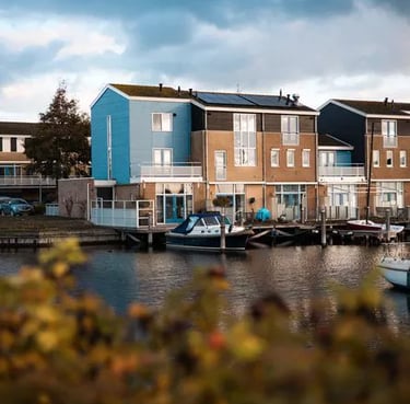Moderne Häuser am Wasser mit privaten Bootsanlegestellen und Solaranlagen unter einem bewölkten blauen Himmel.