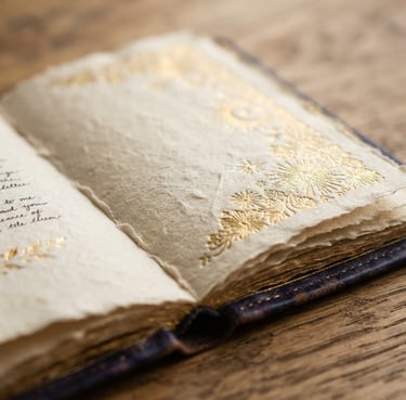 Close-up macro shot of textured linen paper, an open gold-embossed journal, soft morning window light casting gentle shadows