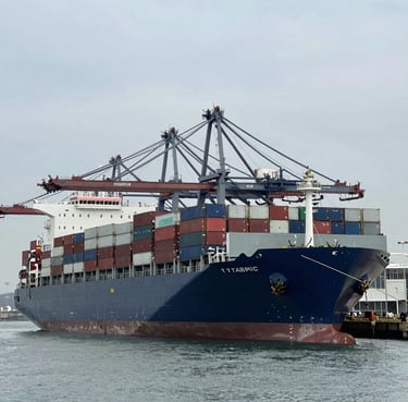 Wide-angle environmental shot of a massive container ship docked at a modern architectural port, cool crisp daylight, steel gray tones