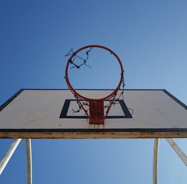 Low‑angle view of a weathered basketball hoop mounted on a white backboard against a clear blue sky 