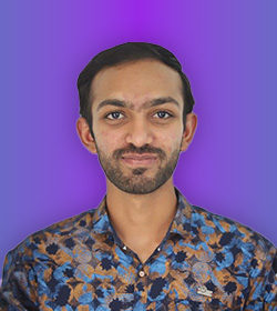 Professional portrait of a smiling man with a beard wearing a blue patterned shirt against a purple background.