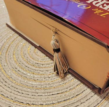 A thick hardcover book with a decorative tassel bookmark resting on a textured circular placemat.