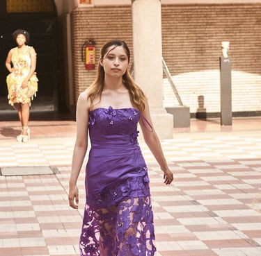 A model walks a runway in a purple strapless gown with a floral lace skirt during a fashion show.