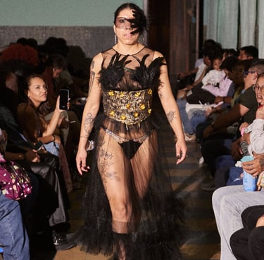 A model walks a fashion runway wearing a bold red structural top and a sheer tulle skirt.