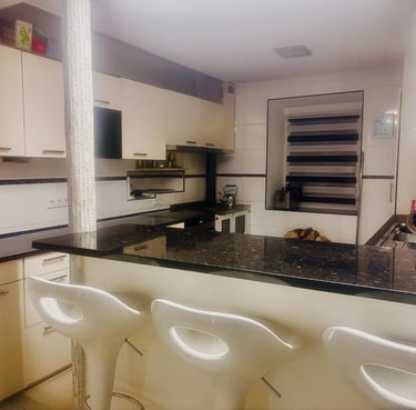 Cuisine moderne avec comptoir en granit noir, armoires claires et tabourets blancs.