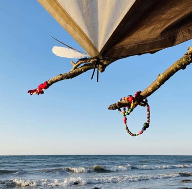 Handmade bead bracelets and colorful ribbons hanging from a tree branch on a sunny beach.