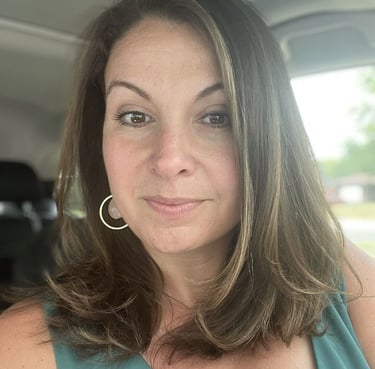 A smiling woman with brown hair and hoop earrings sitting in a car.