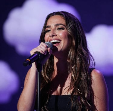 A portrait of a laughing woman singing into a microphone. She is surrounded by a soft bokeh of deep midnight indigo and pale cloud lavender lights. The style is candid and warm.
