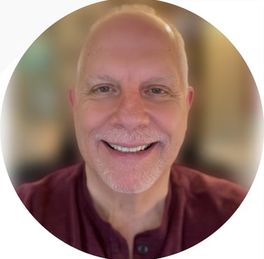 Headshot of a smiling bald man with a grey goatee wearing a maroon shirt.