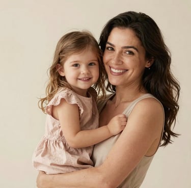 Portrait of a smiling mother holding her young daughter who is wearing a pale dusty rose dress, studio lighting, soft cream background.