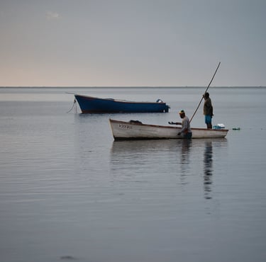 Fishermen at Petite Case Noyale on a traditional wooden boat in calm waters of Mauritius, reflecting the serene early morning