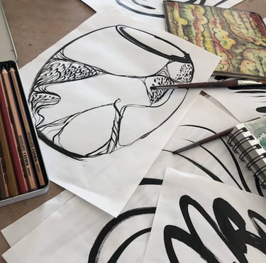 A display of black ink drawings with a vase sketch on top, pencils and notebook