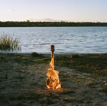 Guitarra en llamas sobre la orilla de un lago al atardecer.