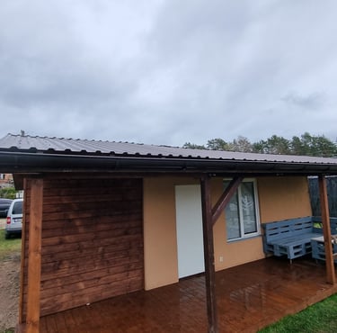 sodo namelis, prie kurio yra termo medienos terasa, sandėliukas malkoms susidėti ir stogas