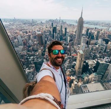 A smiling man takes a selfie with the Empire State Building and New York City skyline view.