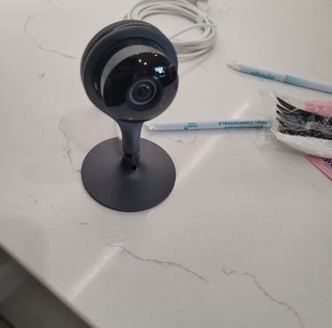 A black Google Nest Cam indoor security camera standing on a white marble countertop.