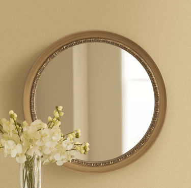 Elegant round wall mirror with an ornate gold frame hanging above white flowers in a vase.