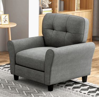 Modern grey tufted armchair with fabric upholstery in a living room setting with a patterned rug.