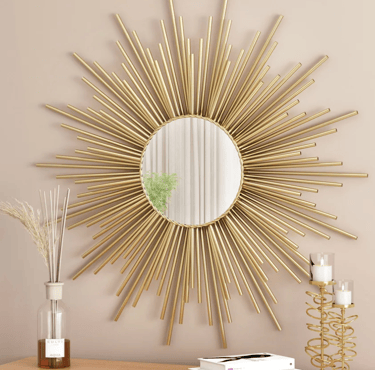 Elegant gold sunburst wall mirror hanging above a table with candles and a glass vase decor.