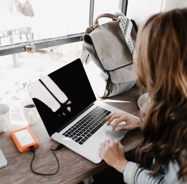 a woman sitting at a desk with a laptop, writing a blog and creating content for brands