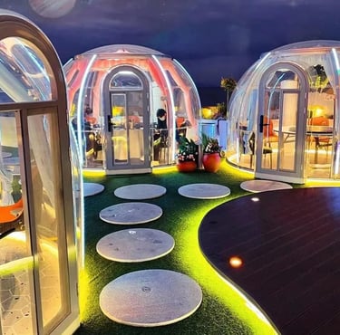 صف من الغرف الزجاجية المضاءة ليلاً في فضاء طبيعي واسع، مخصصة لجلسات طعام عائلية وخاصة