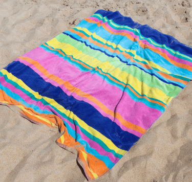 A brightly coloured striped towel lies on sand