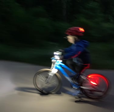 Mały chłopiec na kolorowym rowerku jedzie po ulicy wieczorem.