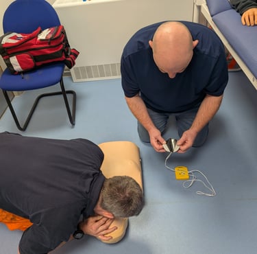 Two men practicing life-saving CPR and AED trainer pad placement on a medical manikin during a first aid course.