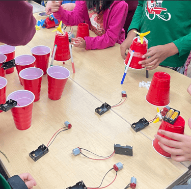 a group of students gathered around a table building drawing bots