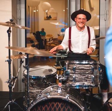 a man in a hat and suspenders playing drums