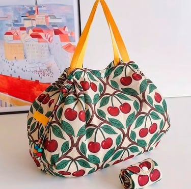Reusable grocery bag with a vintage cherry print and yellow handles next to its folded pouch.