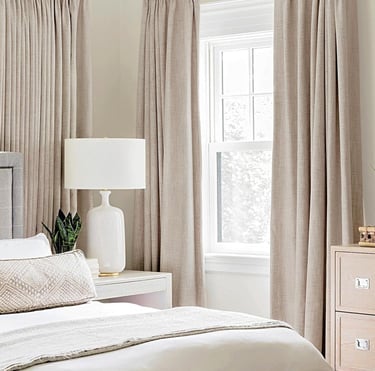 Elegant bedroom interior with neutral linen blackout curtains, white table lamp, and cozy bedding.