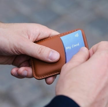 2 hands pulling a digital business card out of a stylish leather card holder on a blurry grey cloud background