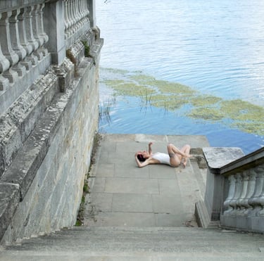 Film still from "Abandonment" by Tina Bikic of a performer lying on wet stone steps beside a lake with green algae.