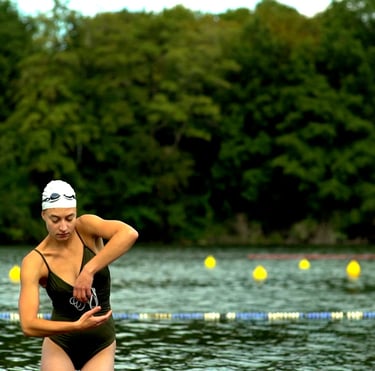Film still from "Belonging" by Tina Bikic showing a woman standing by the water with trees in the background.