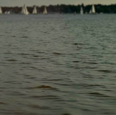 Film still from "Desire for Belonging" by Tina Bikic of a woman dancing through water with sailboats in the distance.