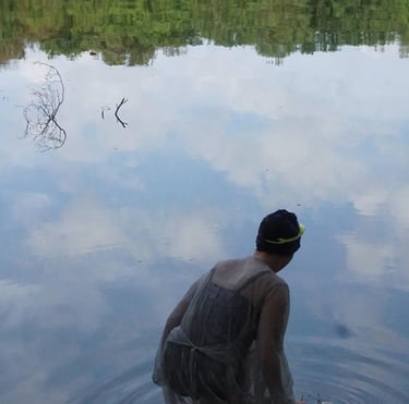 Film still from "Fear" by Tina Bikic showing a swimmer in a dark cap facing the water’s reflection, with clouds mirrored.