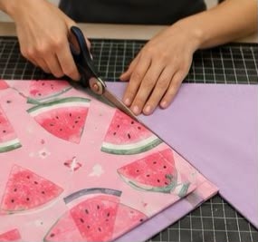 Manos utilizando tijeras de costura para cortar tela de algodón con estampado de sandía.