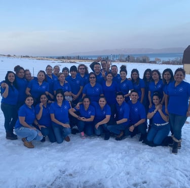 A diverse group of coworkers in blue shirts posing for a team photo in the snow with a lake view.