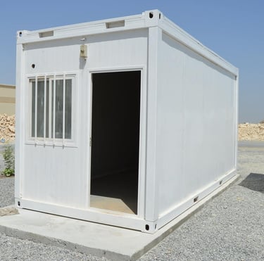 A white portable modular container office with a window and open door on a construction site.