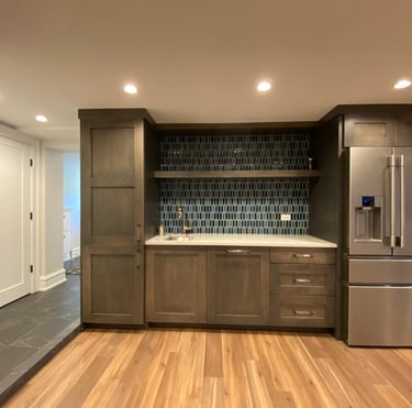 Basement wet bar with natural stone countertop, tile backsplash, and built-in storage cabinets