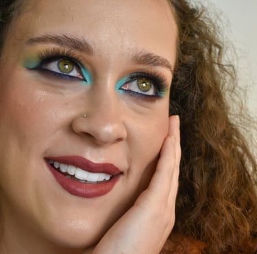 Una mujer con cabello rizado que usa sombras de ojos azules y amarillas vibrantes y un lápiz labial