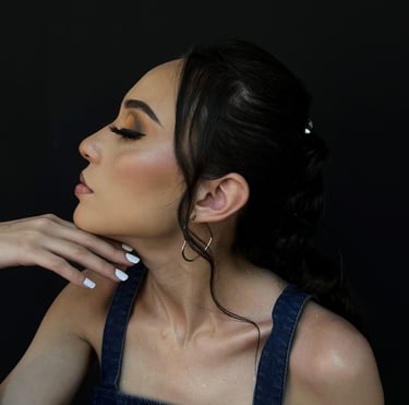 Perfil lateral de una mujer con sombra de ojos de atardecer y un top de mezclilla sobre un fondo neg