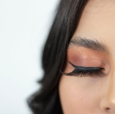 Primer plano de una mujer con sombra de ojos color bronce, delineador de ojos negro y pestañas posti