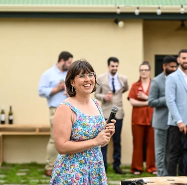 Laura smiles as she looks off camera. She is holding a microphone as she MC's a wedding