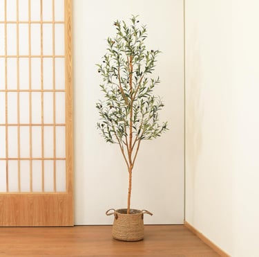 Tall artificial olive tree in a woven seagrass basket planter against a white wall and shoji screen.