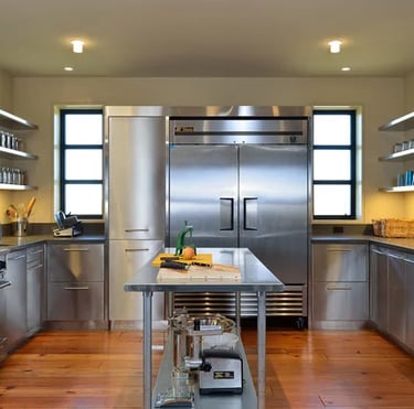 A modern home kitchen featuring a stainless steel table used as a central prep island with matching cabinetry and appliances.